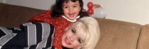 Jayne Mansfield lying on a couch with her young daughter Mariska Hargitay smiling on her back, holding a balloon in 1985.